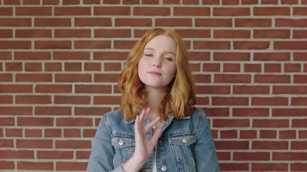 retrato de una hermosa mujer de cabello rojo con confianza en el fondo de la pared de ladrillo corriendo de la mano a través del cabello