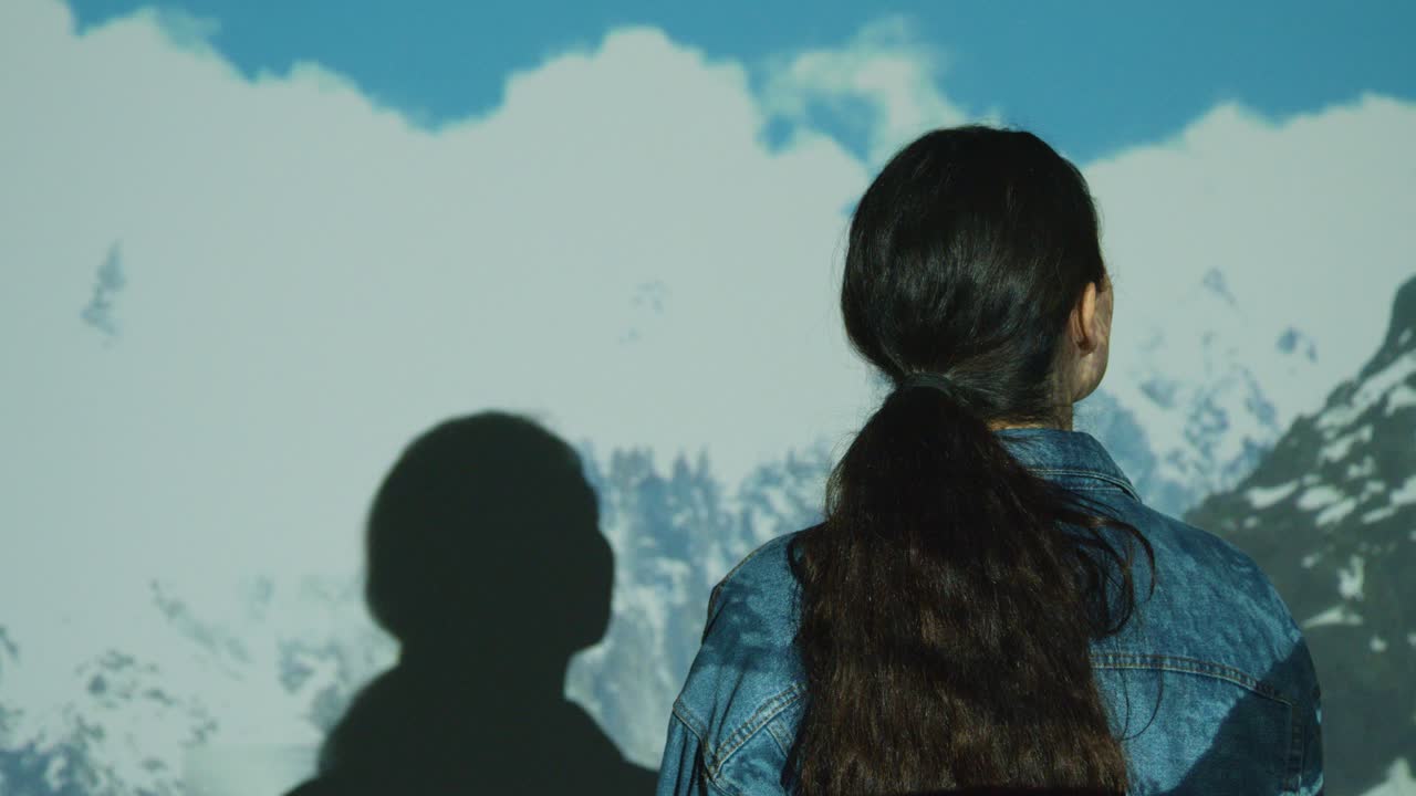 구름과 산의 이미지가 그녀의 몸에 투사되는 몰입 예술 전시회를 방문하는 여성