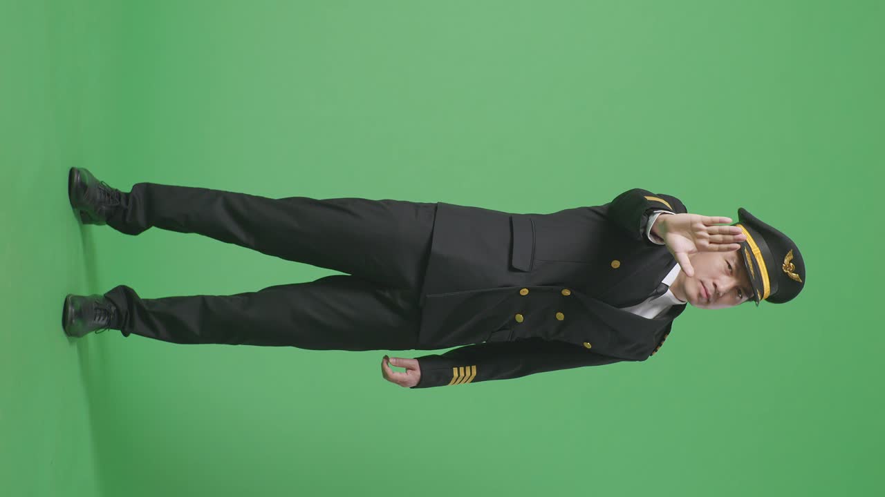 아시아 남성 조종사가 카메라를 바라보고 녹색 스크린 배경 스튜디오에서 손 표시 없이 불쾌감을 표합니다.