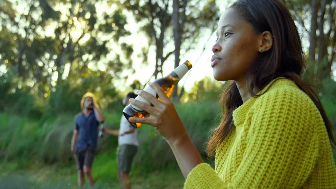 Thoughtful young woman drinking beer in the forest 4k