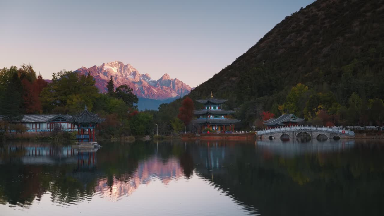 La prima luce del sole dipinge di oro la montagna Yulong mentre la Pozza del Drago Nero riflette i tradizionali padiglioni, i ponti ad arco e l'acqua calma in una serena scena all'alba