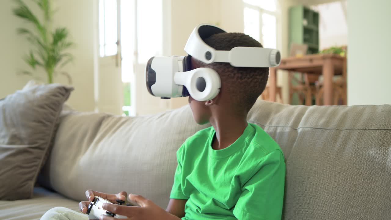 Bambino afroamericano seduto sul divano con visore VR e controller, che reagisce alla realtà virtuale, con spazio per il testo
