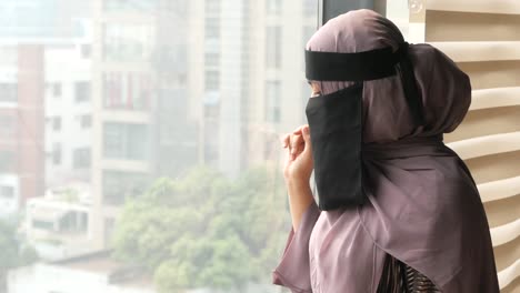 mujer con hijab y niqab mirando por una ventana