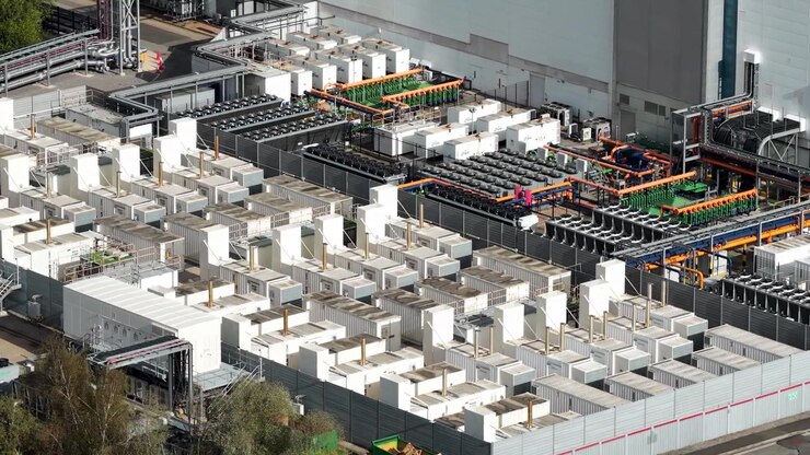 Aerial drone shot of a large data center power and cooling area, showing backup generators, fan banks, pipework and industrial equipment in Newport, Wales.