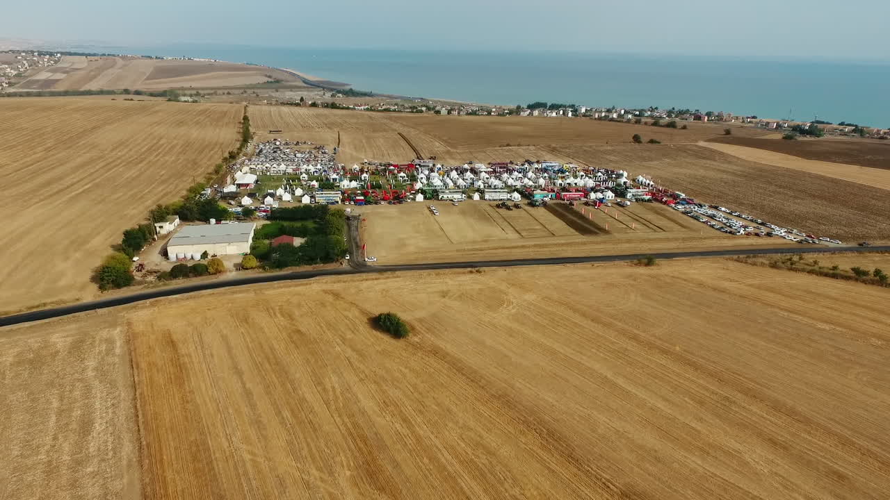 Drönarbild med fågelperspektiv över en lantbruksmässa på gula fält av åkermark med öppen blå himmel