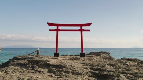 paisaje tranquilo y relajante con puerta torii japonesa contra el océano en la parte superior de la roca