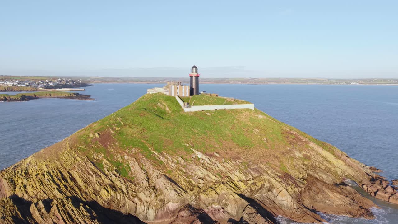 Ballycotton lighthouse sits on a rocky island with green grass, surrounded by blue sea