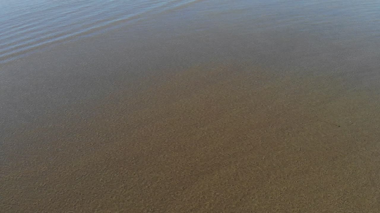 Waves moving across dark sand in Bali on the west coast