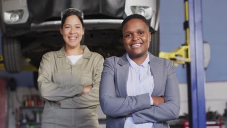 Video-of-two-diverse-happy-female-car-mechanic-and-business-owner-looking-at-camera