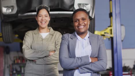 video of two diverse happy female car mechanic and business owner looking at camera