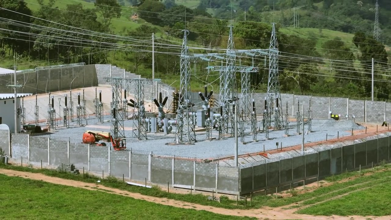 High voltage electrical substation with transformers, switchgear and transmission infrastructure near Santo Antônio do Monte, Minas Gerais, Brazil surrounded by pastureland, drone pullback parallax