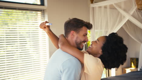 pareja emocionada en el dormitorio en casa celebrando el resultado positivo de la prueba de embarazo