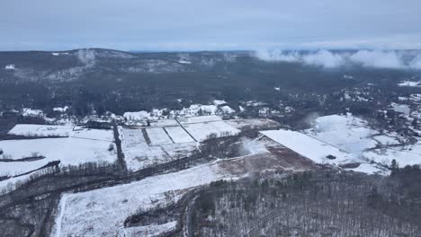 Volando-Sobre-Tierras-De-Cultivo-Cubiertas-De-Nieve-Sobre-Un-Valle-De-Montaña-En-Un-Día-Nublado-De-Invierno