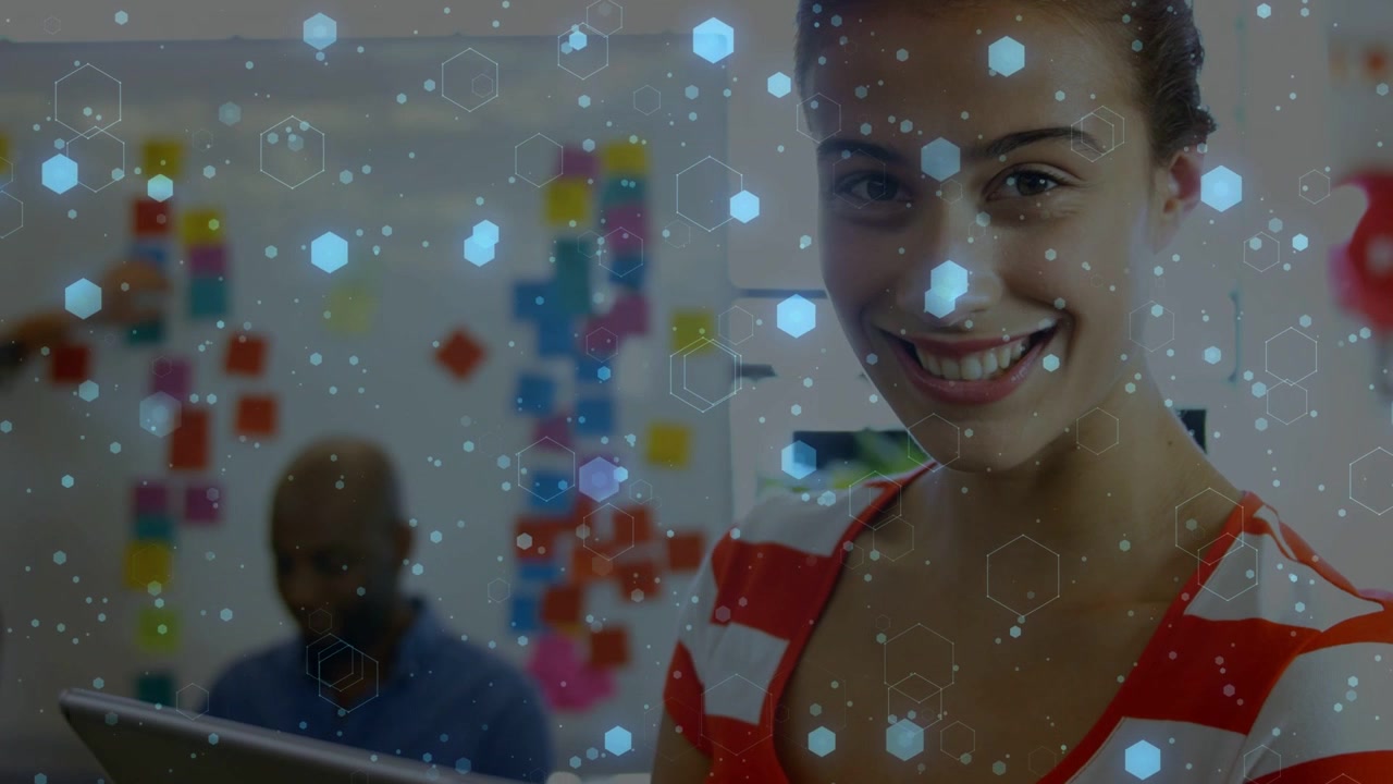 Woman reading tech data on tablet looking up smiling while blue hexagons overlaying tablet and desk