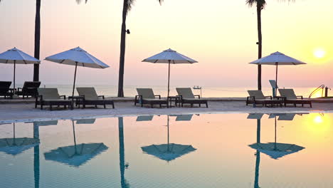 as the sun sets over the ocean beach umbrellas reflect in a resort pool