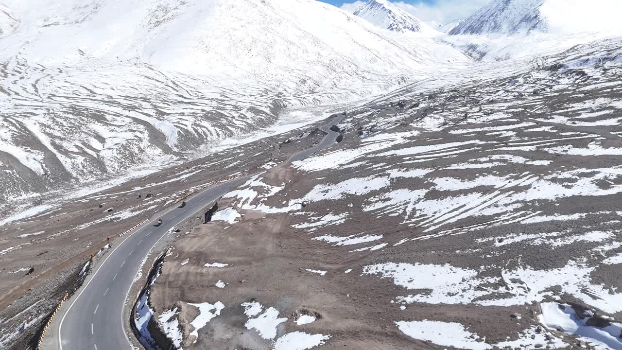 Aerial drone shot following a lone car on an endless highway stretching through Ladakh’s stark and vast landscape.