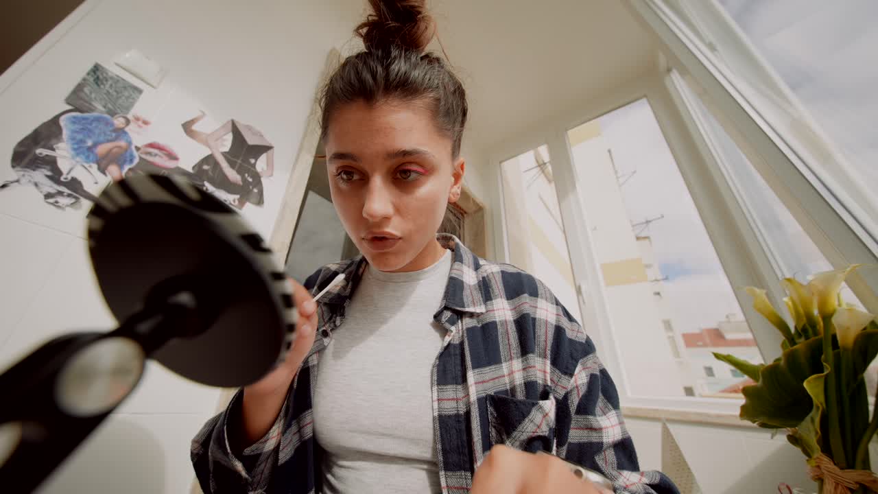 Giovane donna che applica l'eyeliner e fa smorfie allo specchio.