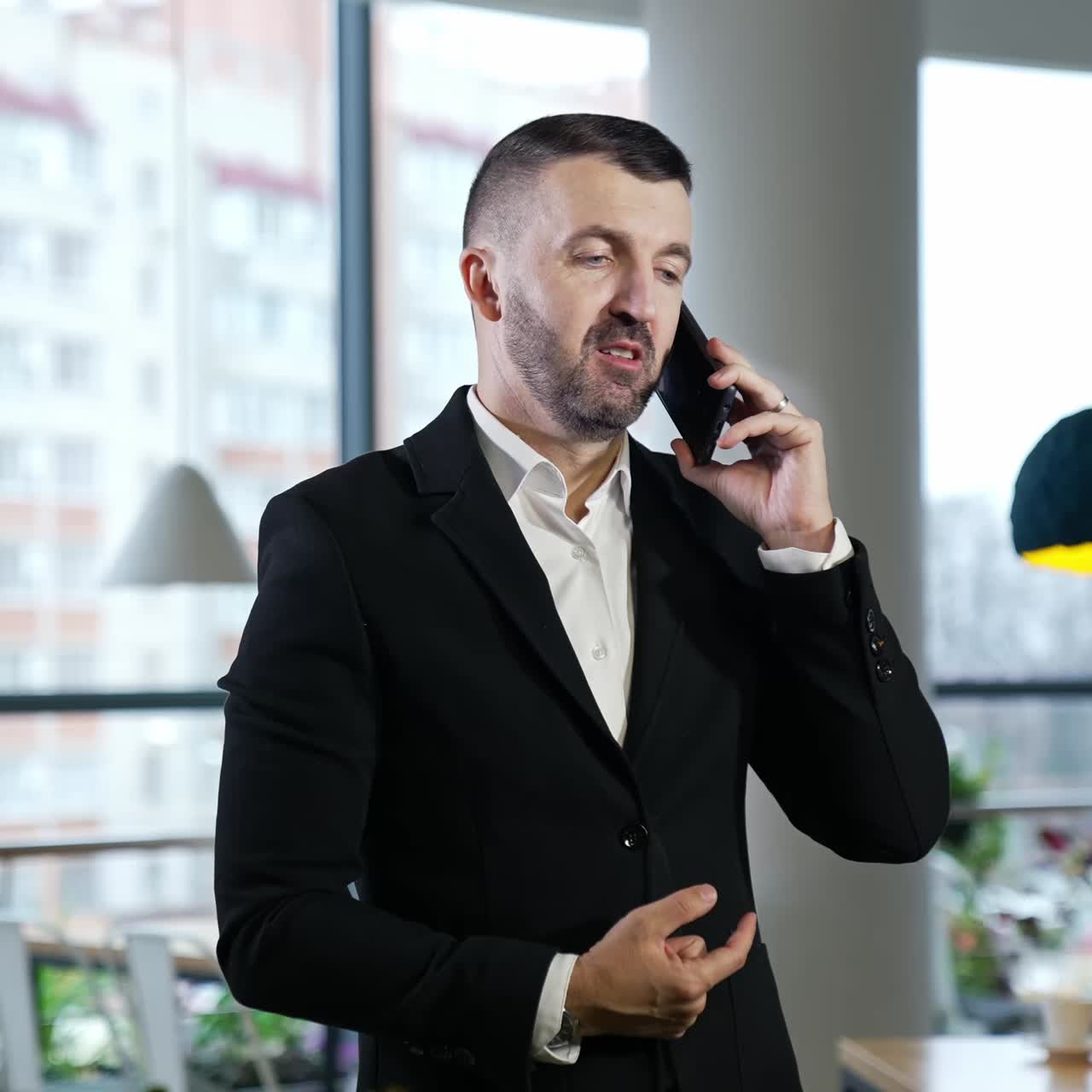 Businessman having a pleasant conversation on the mobile phone. Confident man has business talk on the phone. Big windows at the backdrop