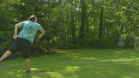 a man makes an approach shot in a shaded, wooded area aiming for the disc golf basket, illustrating skill and precision in the sport