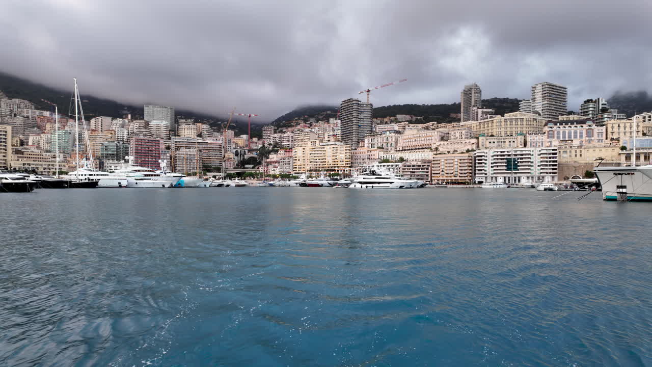 La Condamine, Monaco - July 4, 2025: Row of sleek luxury yachts, docked in Port Hercules with the Monaco cityscape and misty hills in the background