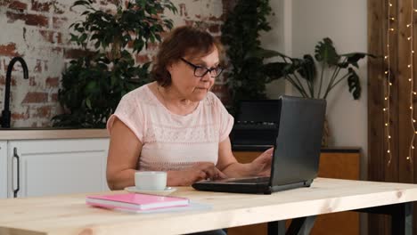 una mujer madura senior usando una computadora portátil en la cocina.