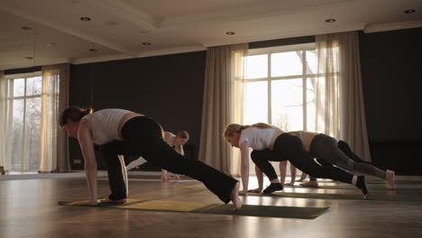 a group of women practice yoga under the strict guidance of an instructor in slow motion and sunlight at sunrise.