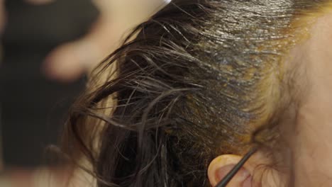 At-the-salon,-a-hairstylist-applies-bleach-paste-on-several-layers-of-woman's-hair