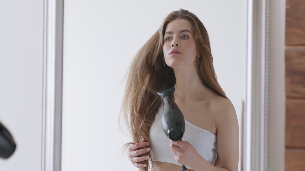 Mujer secándose el pelo frente a un espejo