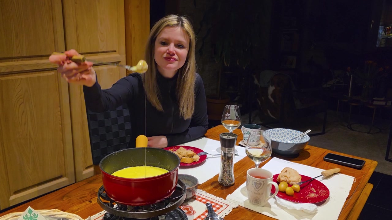 Traditional Swiss cheese fondue meal at home, young woman enjoys a cosy dining experience with melted cheese, bread and classic comfort food in a warm indoor setting