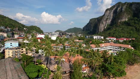 Luftdrohne-Fliegt-über-Große-Kokospalmen-Und-Enthüllt-An-Einem-Sonnigen-Sommertag-Die-Stadt-Ao-Nang-In-Krabi,-Thailand,-Mit-Großen-Kalksteinfelsen-In-Der-Ferne