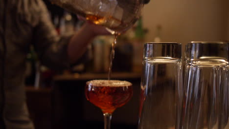 bartender pours whiskey manhattan cocktail into glass on bar