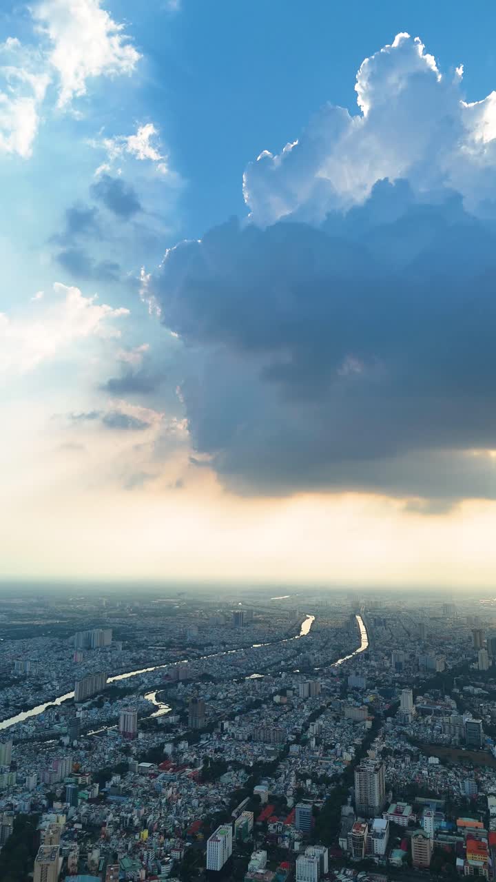 Vertical aerial view over Ho Chi Minh City (Saigon), Vietnam, during sunset, as dramatic clouds cast shadows across the dense urban sprawl.