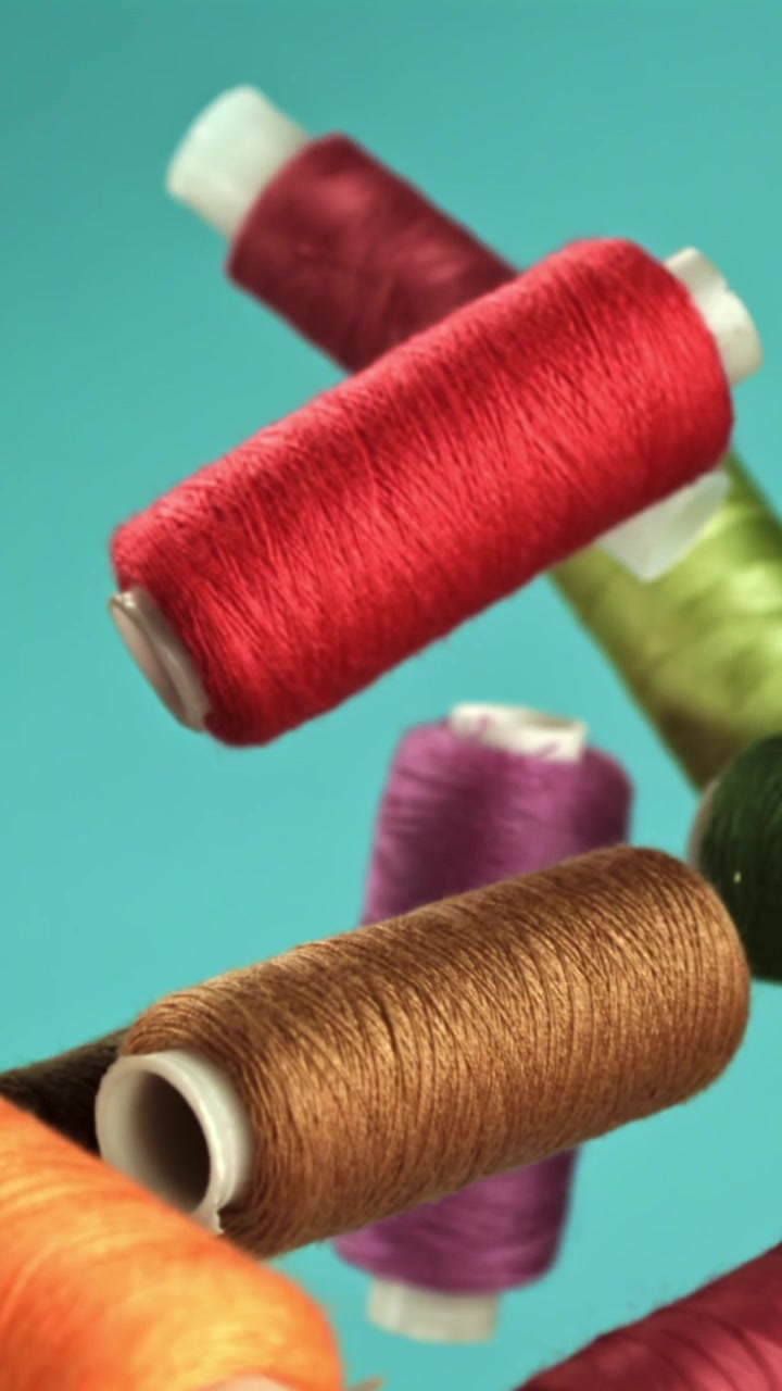 Multicolored Thread Spools Falling in Slow Motion on Teal Background