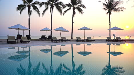 Impresionante-Cielo-De-Puesta-De-Sol-Pastel-Reflejado-En-La-Superficie-Del-Océano-Y-Agua-Tranquila-De-La-Piscina-En-Un-Resort-Isleño-De-Lujo