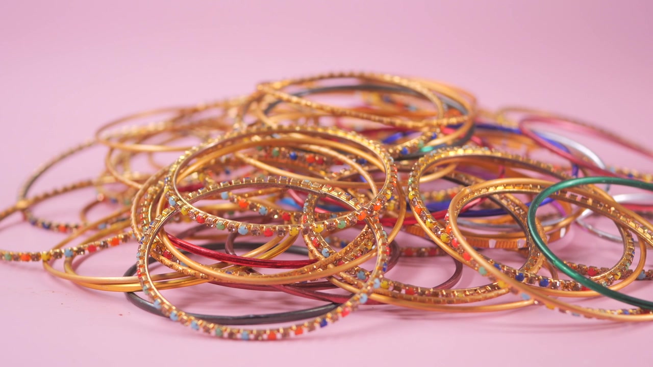 Primo piano di tradizionali braccialetti indiani d'oro e colorati su sfondo rosa