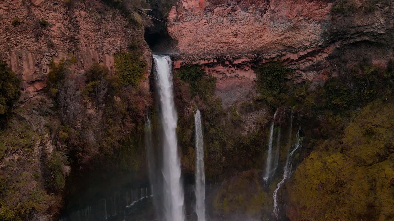 drone aerial of waterfall cascading through narrow canyon slot, Siete Tazas National Park, Ñuble, Chile with dramatic red rock cliffs