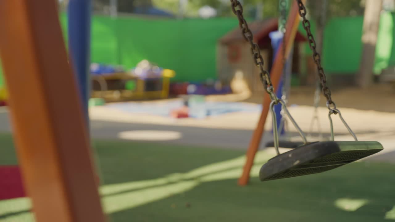 Swing moves gently in sunny playground with no children around. Empty School or Kindergarten closed, neglect, missing child, bullying aftermath, or about safety concerns , supervision, child welfare