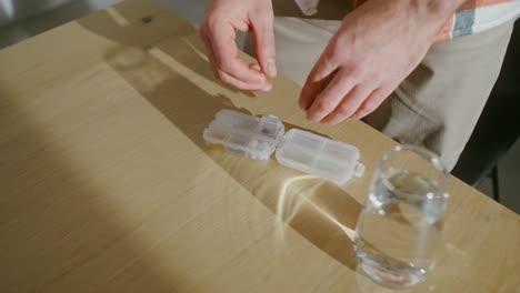 person taking medicine with pill organizer and water