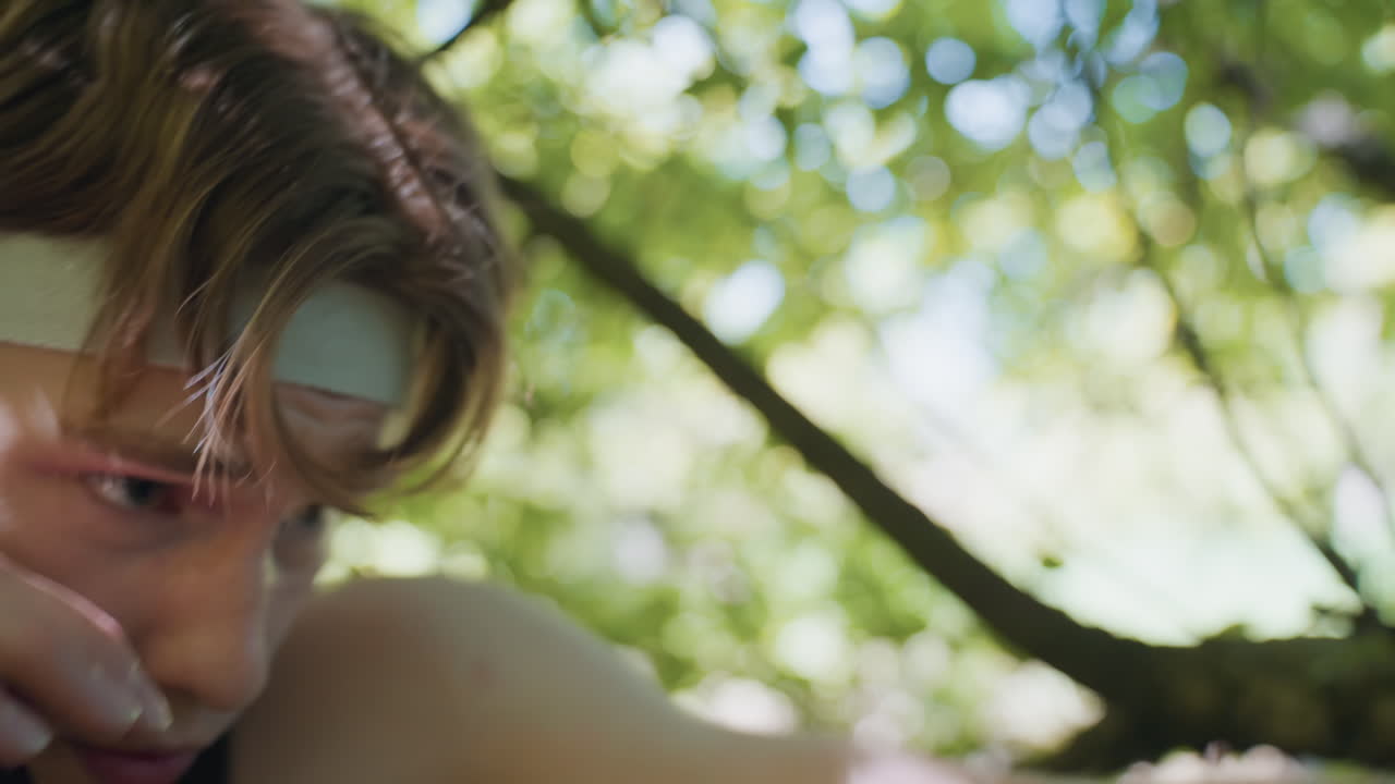 close up tense Adventurer face in headband dodging forest branches while delivering harsh punches with intense gaze and clenched jaw muscles glistening with sweat dynamic action in woodland arena