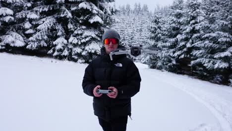 person holding a drone in a snowy forest environment