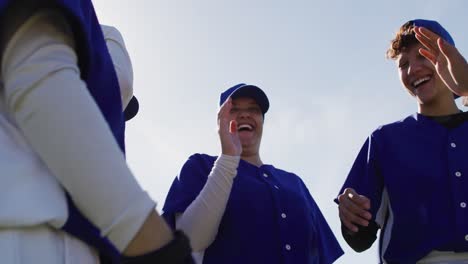 Happy-diverse-team-of-female-baseball-players-talking-and-high-fiving-after-game