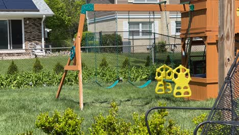 An-empty-swing-in-a-suburban-home-backyard-on-a-sunny-day,-time-lapse