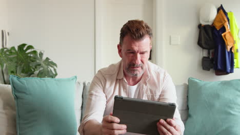 Senior man at home using tablet, expressing surprise and excitement