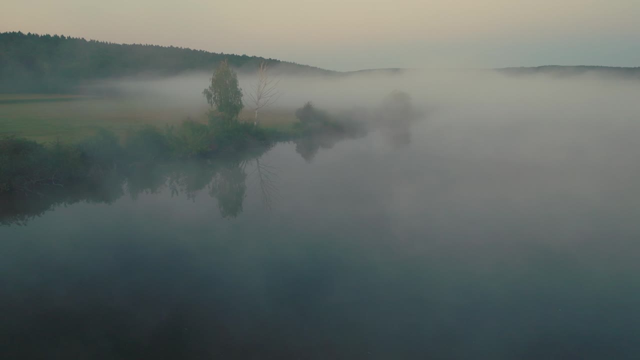 Aerial view of fog over fields and trees, dense mist filling the scene as dusk falls, creating a calm atmosphere