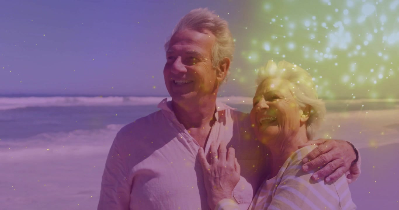 Pareja mayor de pie en la orilla contemplando, riendo mientras destellos dorados entran desde la derecha (anuncio publicitario)