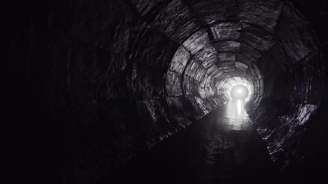 túnel de hormigón de drenaje redondo con agua construido con encofrado. con luz al final. río subterráneo escondido en tubo.