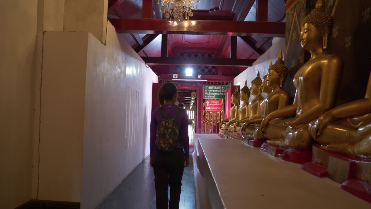 turistas caminando por el templo budista pasando por estatuas de buda de meditación seguidas, tailandia