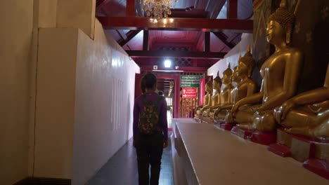 tourists walking through buddhist temple passing by meditation buddha statues in a row, thailand