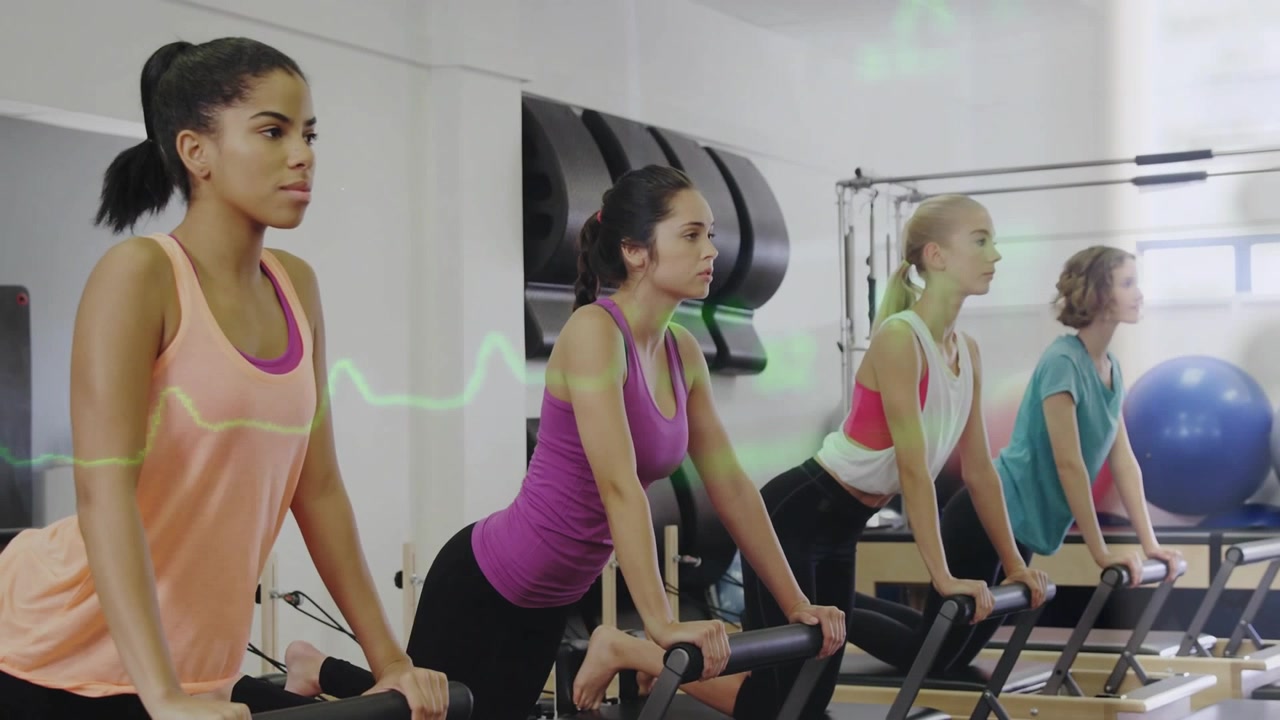 Vertical video: Kneeling women pushing reformers in Pilates studio on breath cue, wearing tanks