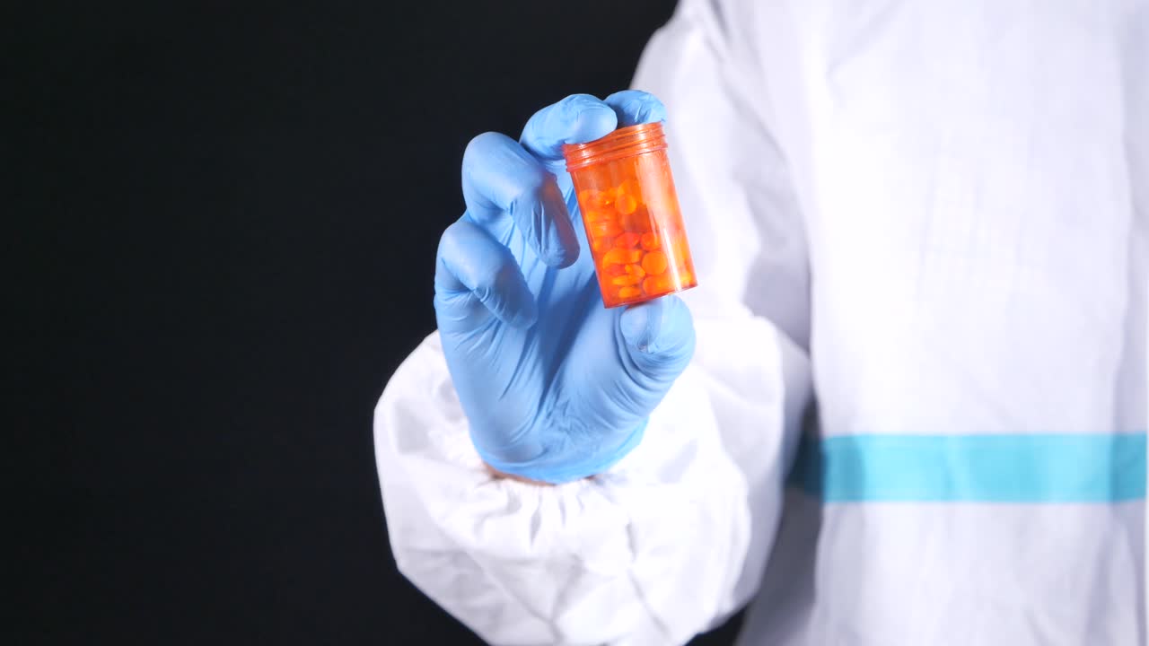 primer plano de una mano con un guante de protección sosteniendo un frasco de pastillas